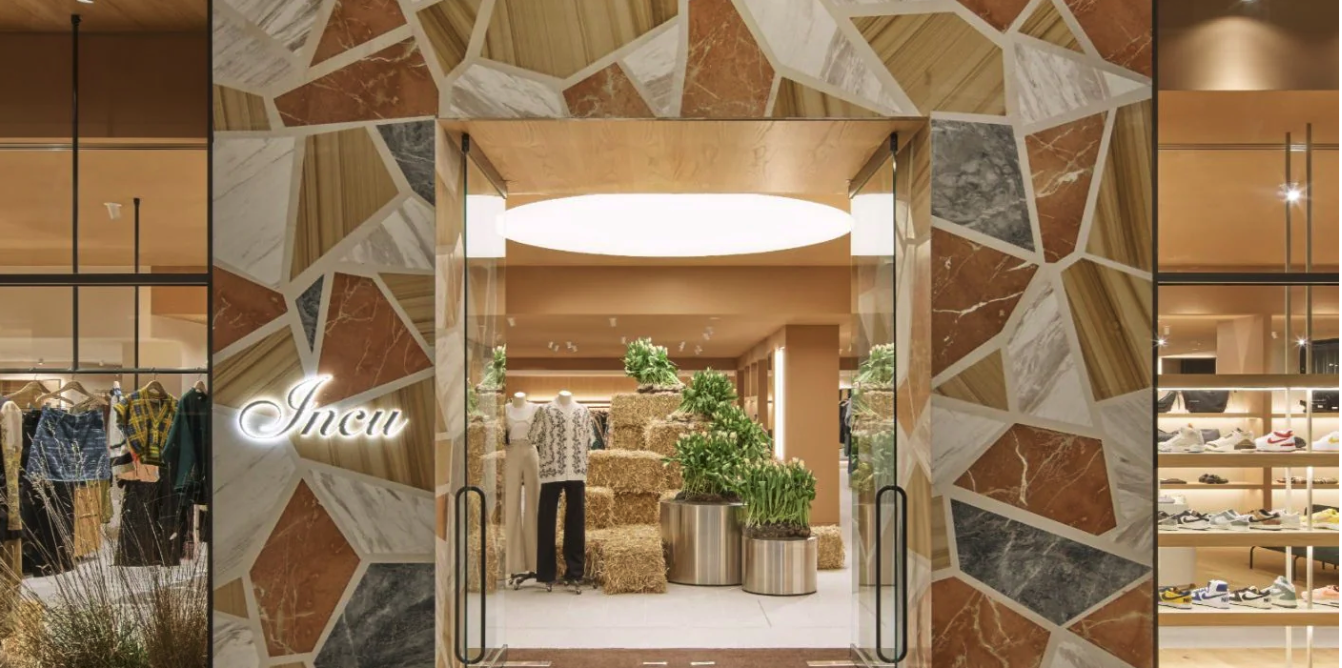 Store entrance with geometric marble wall design, mannequins, and display of clothing and shoes inside.