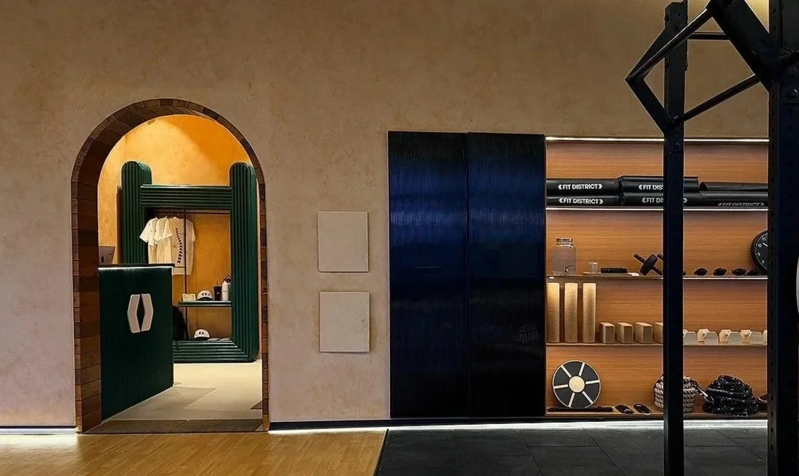 Interior view of a gym or workout space with a doorway leading to what's likely a boutique area, displaying gym apparel, and shelves with workout equipment and accessories.