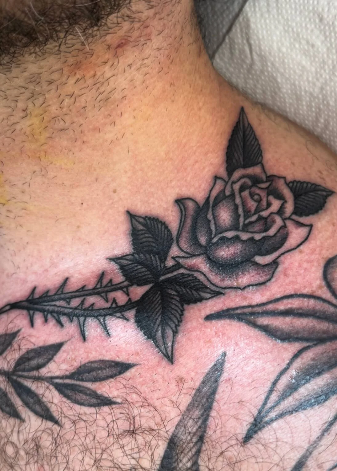 Black and gray tattoo of a rose with leaves on the person's shoulder and chest.