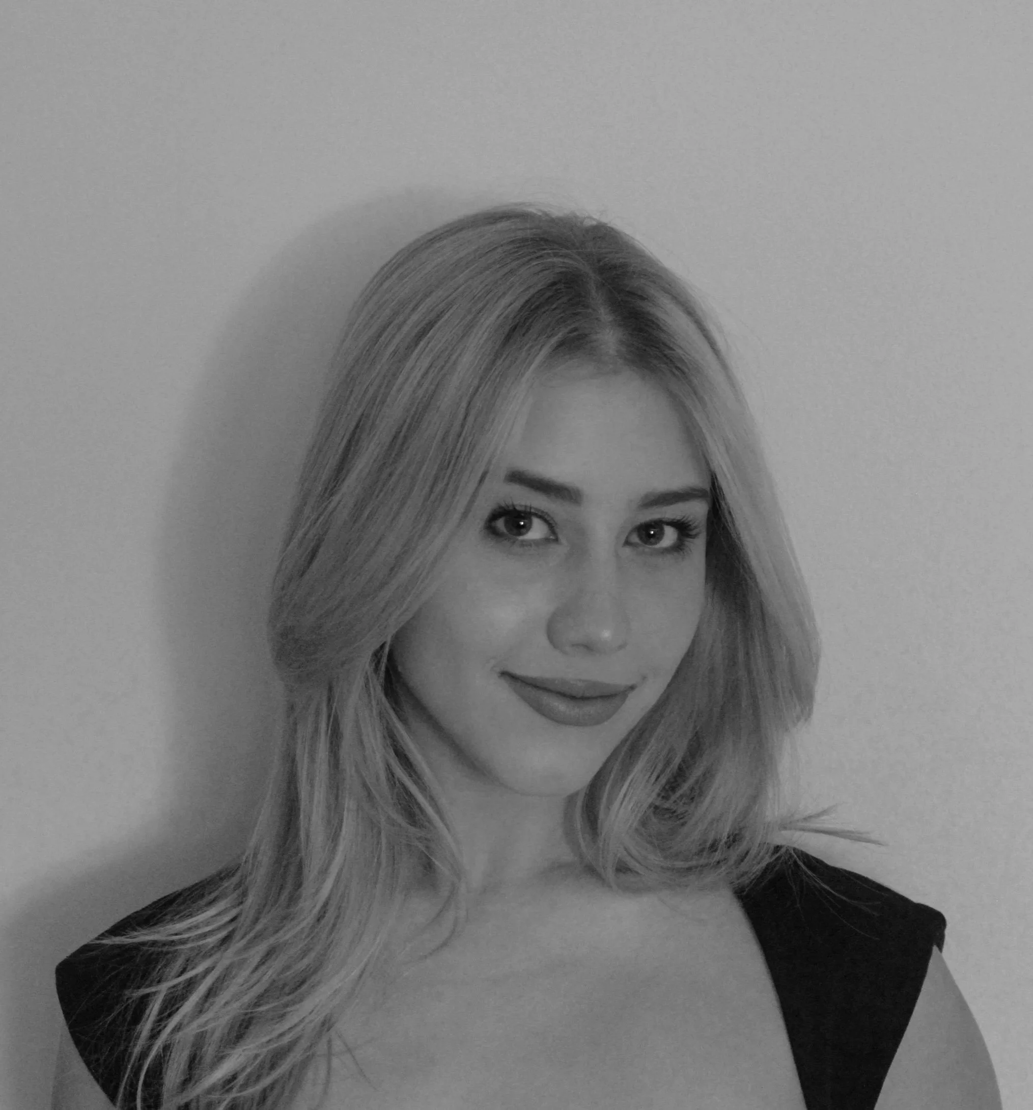 Black and white portrait of a young woman with shoulder-length wavy hair, wearing a sleeveless top, smiling gently at the camera.