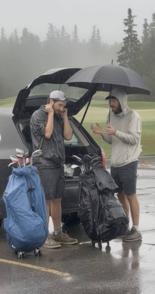 Kaksi miestä sateisella golfkentällä, toisen päällä huppu, toinen varjoja pitäen, avatussa auton takakonteissa ja golfreppu jalassa.