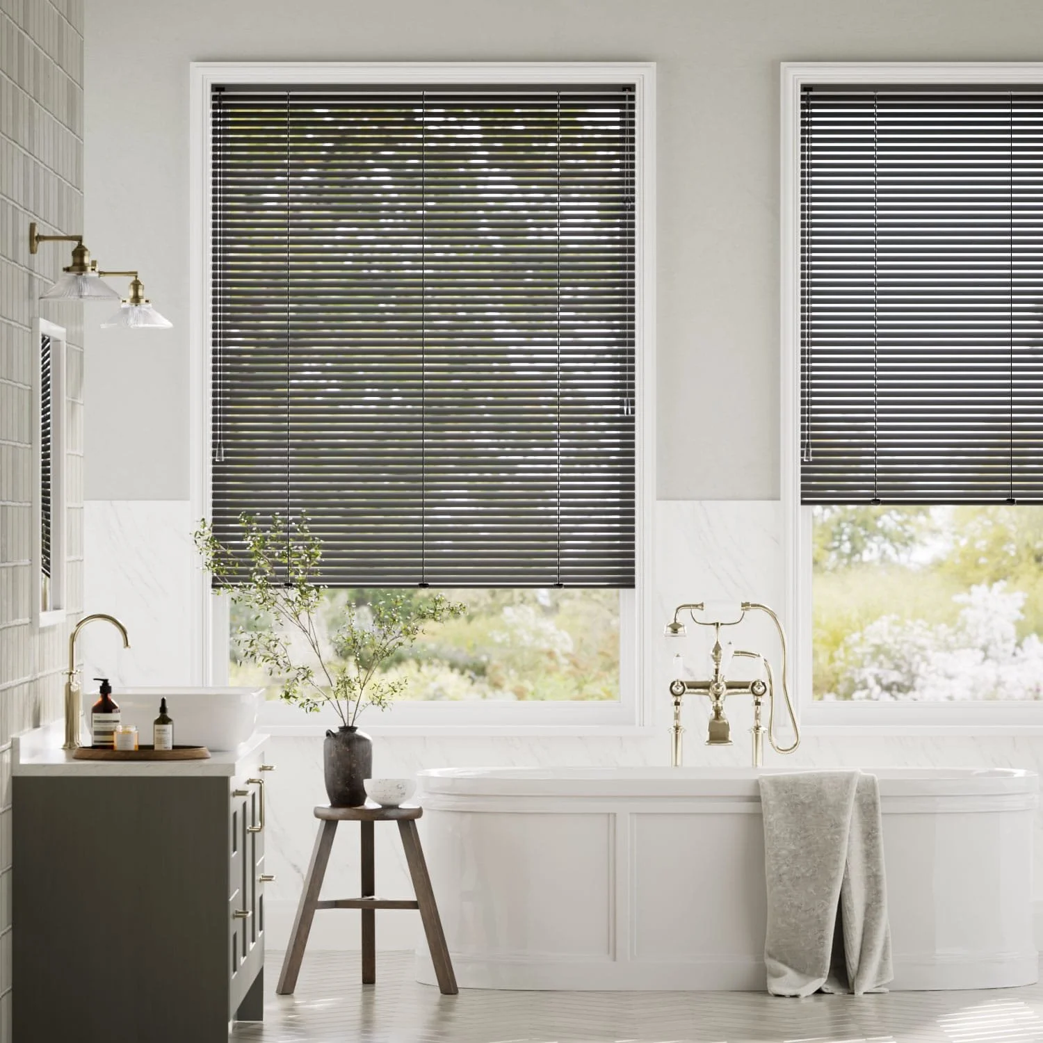 Bright bathroom with large windows, black blinds, white bathtub, gold fixtures, side table with plant, and neutral decor.