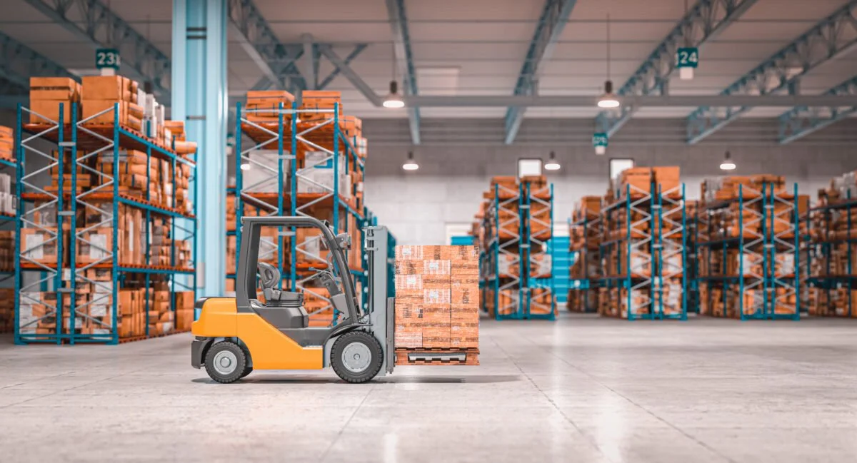 A forklift moving a pallet of boxes in a warehouse with shelves filled with orange and white boxes.