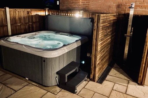 Outdoor hot tub in Cromer with steps, privacy fencing, and a brick wall in the background.