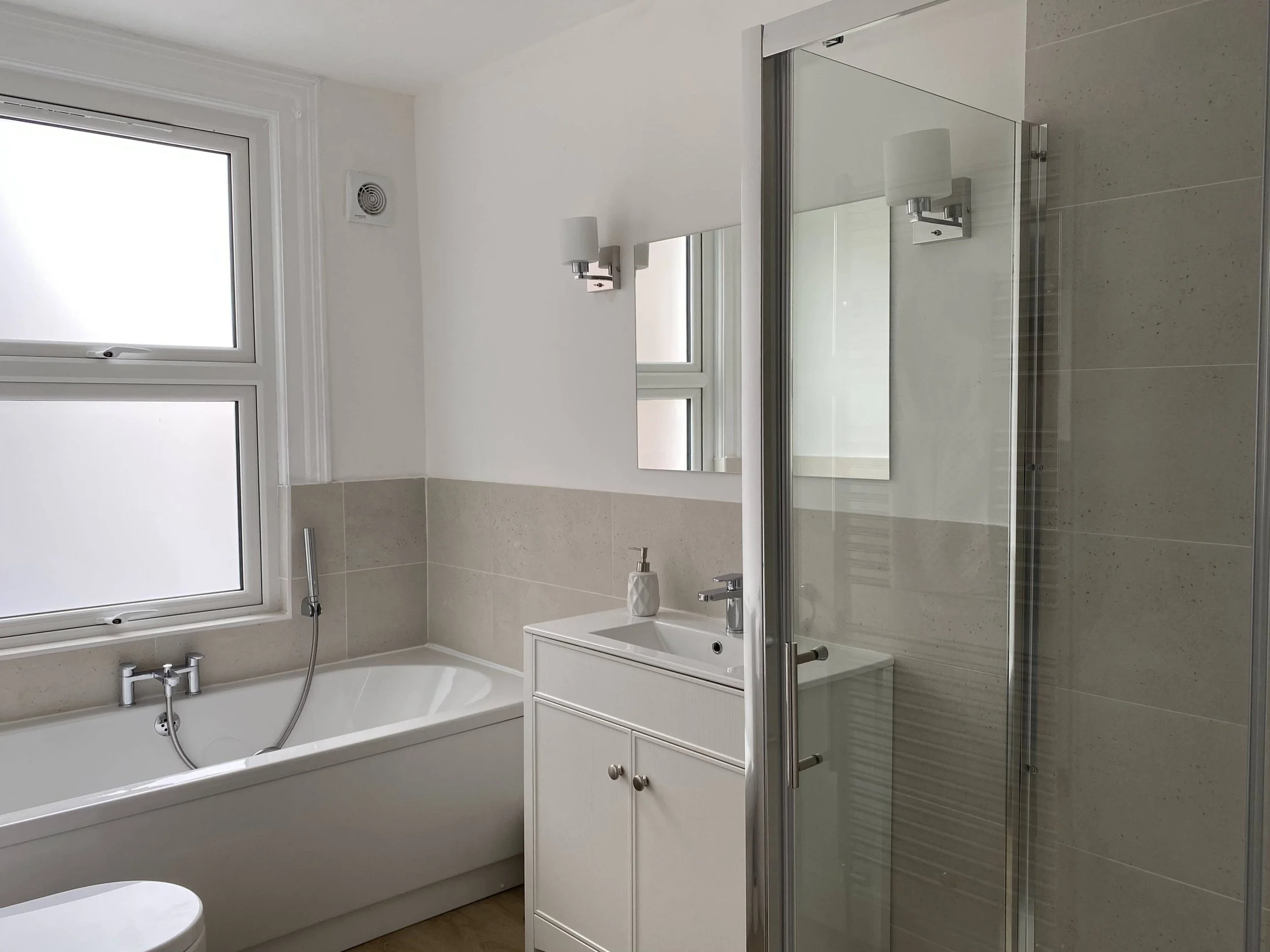 Modern bathroom with a bathtub, a small sink with a cabinet, a mirror, frosted windows, and a glass shower enclosure.