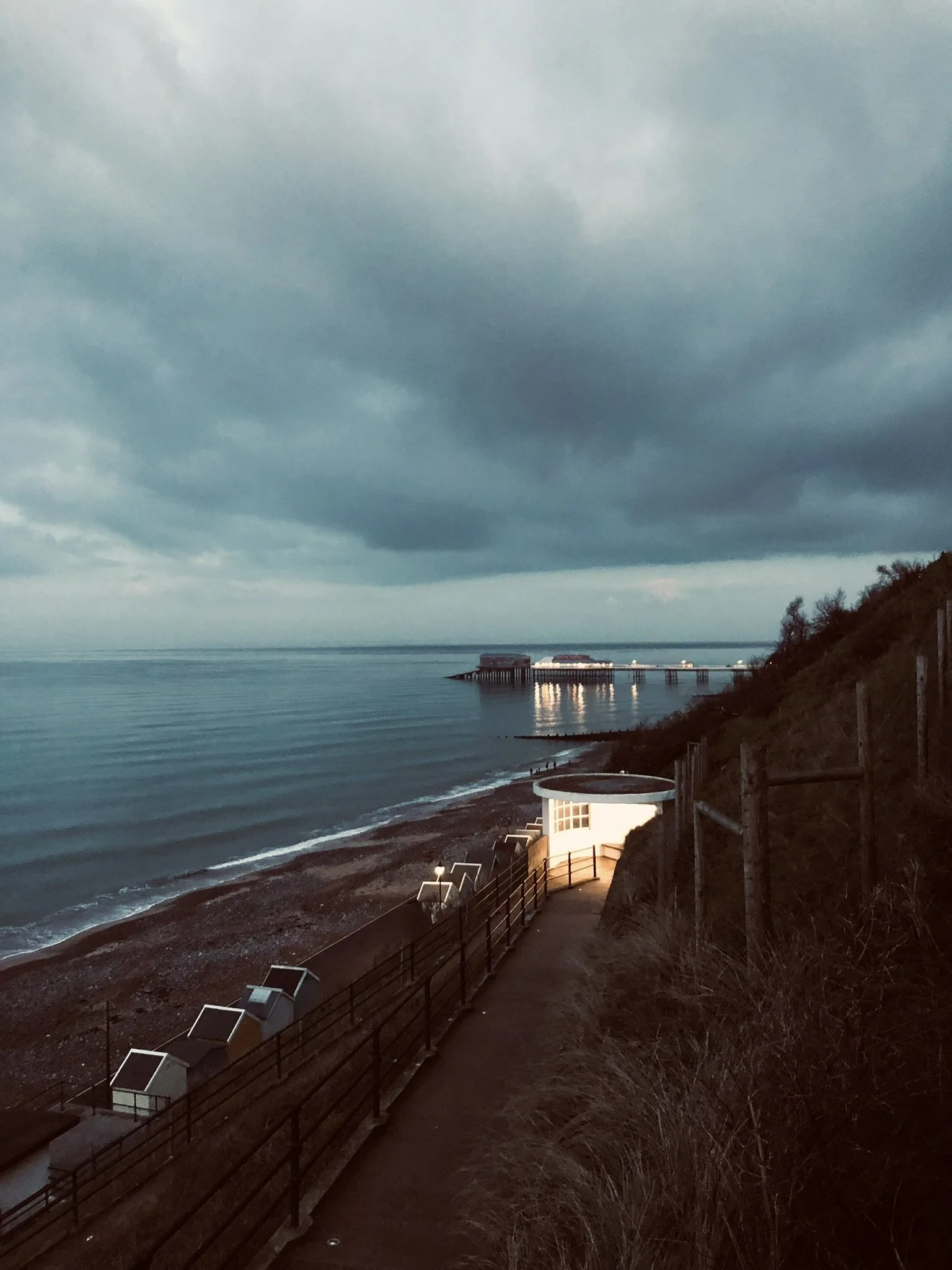 Cromer beach and Cromer Pier  during sunset or dusk, with Cromer Pier in the distance, showing the ramp that leads down to the promonade
