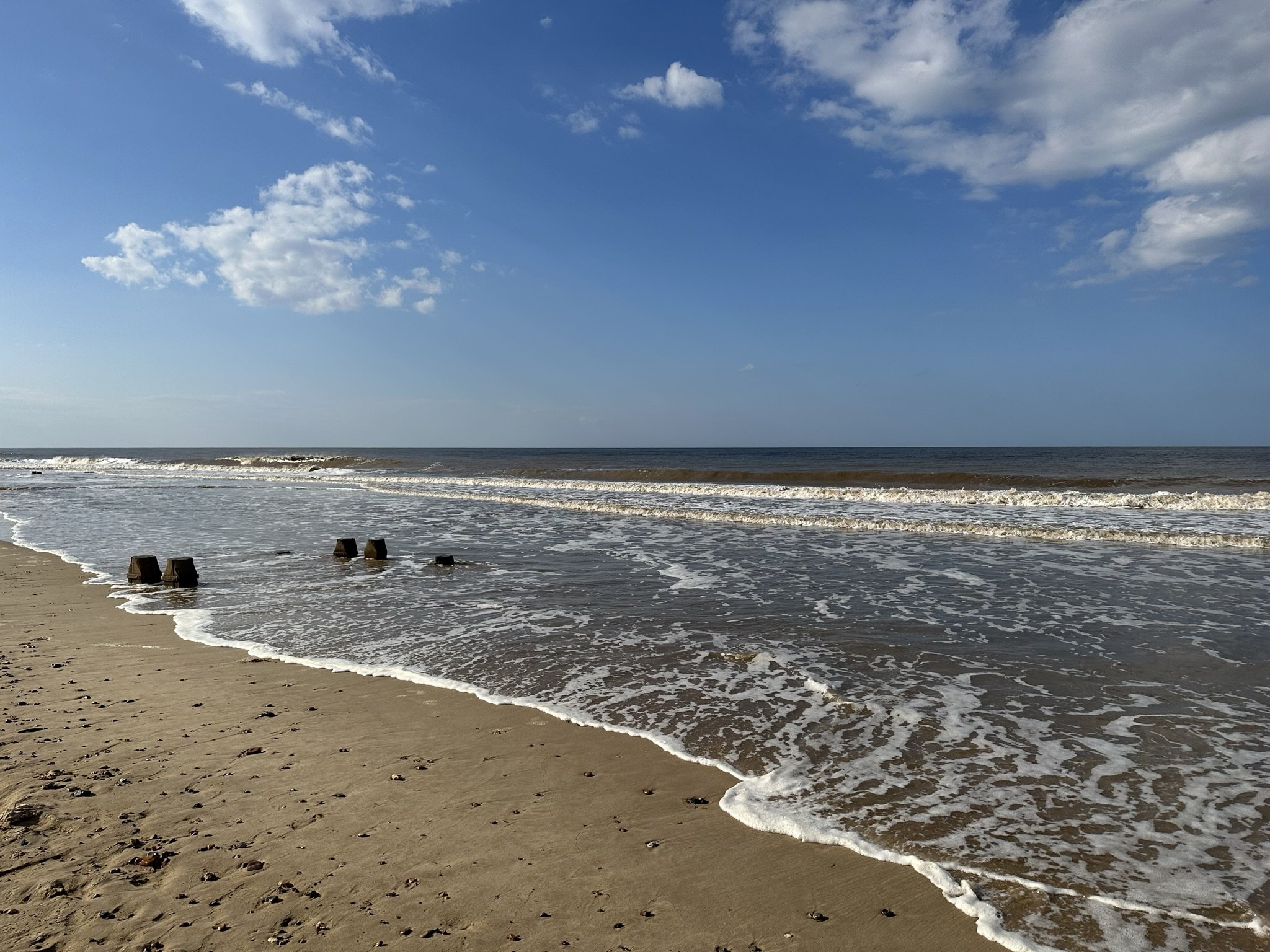 Bacton's sandy beach with gentle waves and a partly cloudy sky.