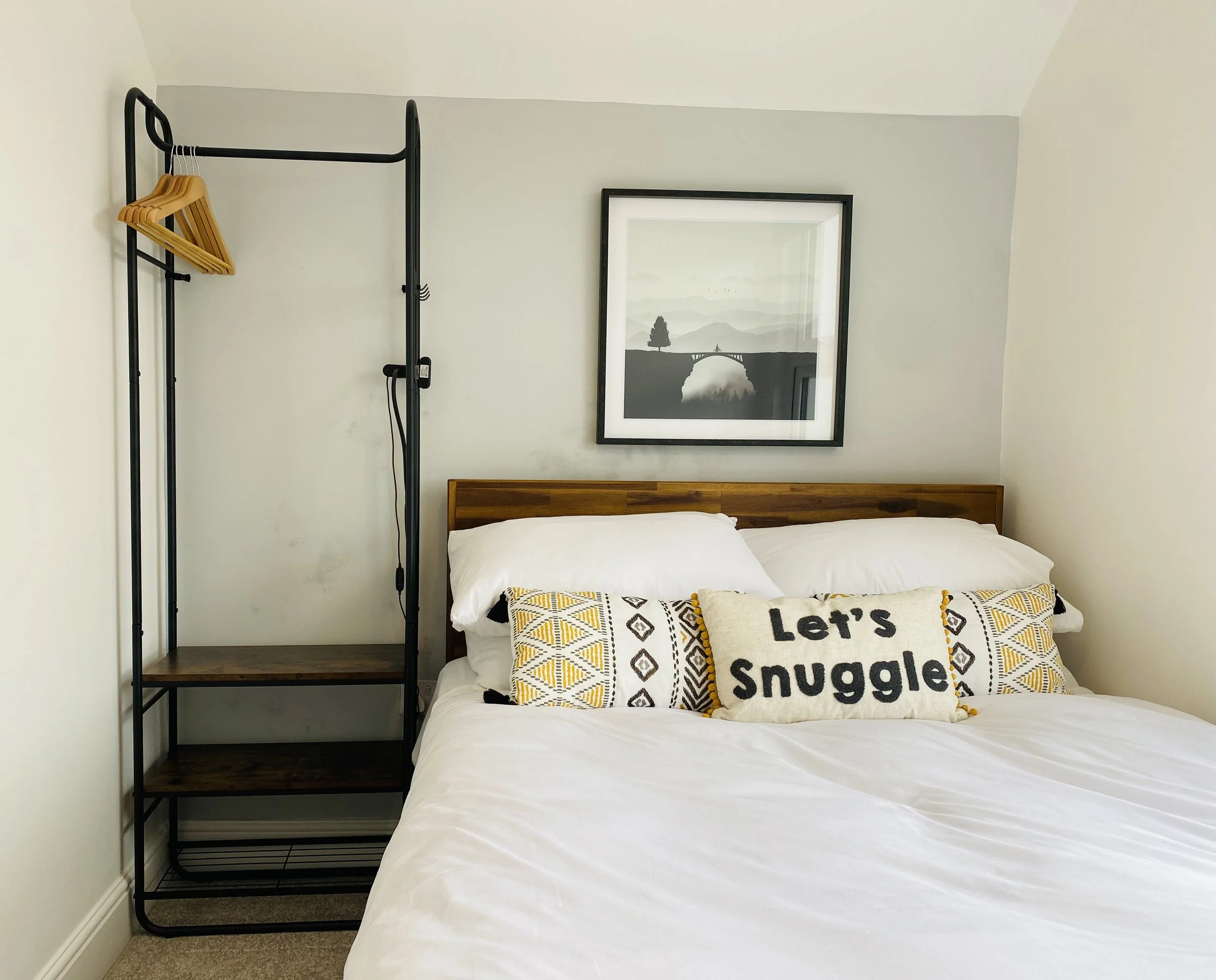 A cosy double bedroom in Coast House, Cromer, featuring a bed with white linens, decorative pillows including one with the text "Let's Snuggle," a wooden headboard.
