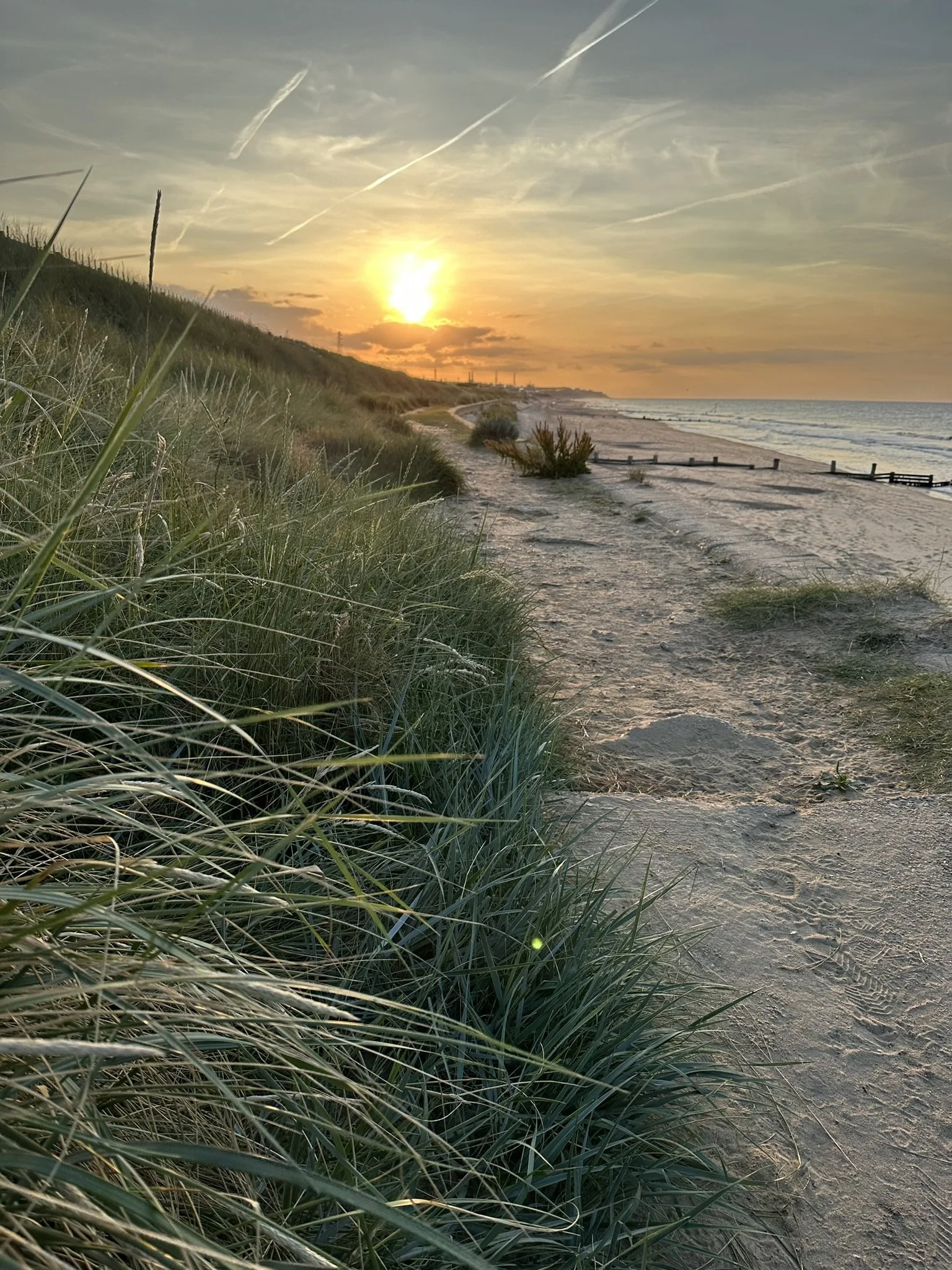 Sunset over a sandy beach at Bacton, North Norfolk, with grassy dunes in the foreground and a calm sea on the right.