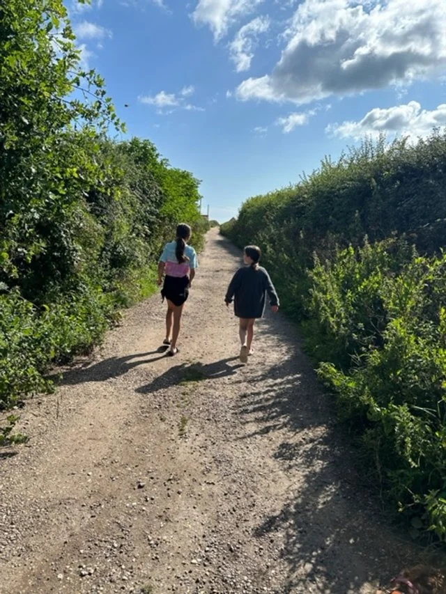 The whole family can walk down a sandy lane that leads directly to Bacton's sandy beach, surrounded by green bushes and trees under a blue sky with some clouds.