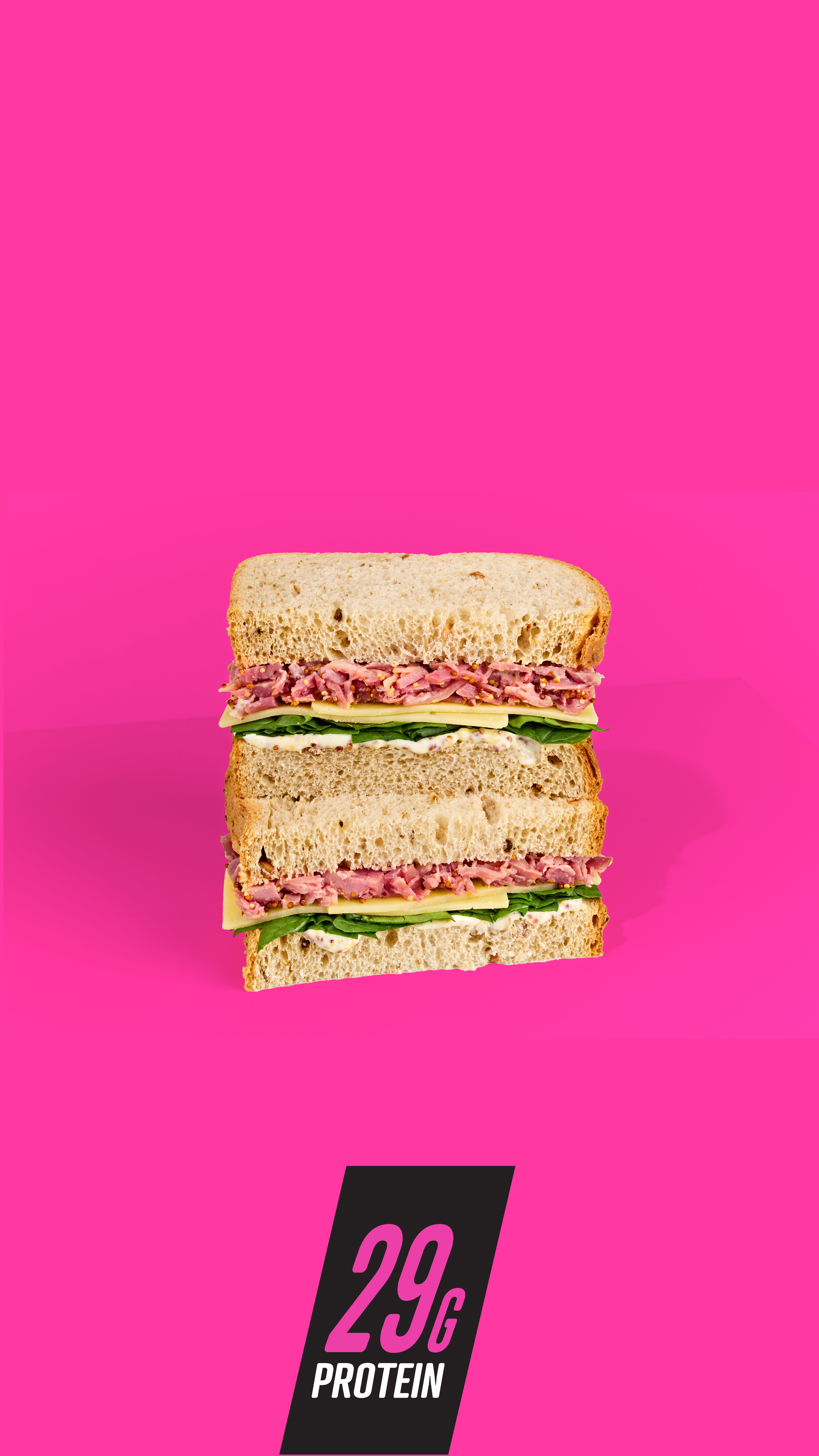 Two sliced sandwiches with ham, cheese, and spinach on a pink background, with a graphic indicating 29 grams of protein