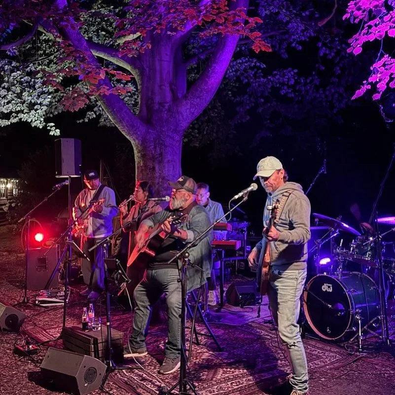 Three individuals standing outdoors on a foggy day, with a woman in the foreground and two men in the background, all dressed in dark clothing.