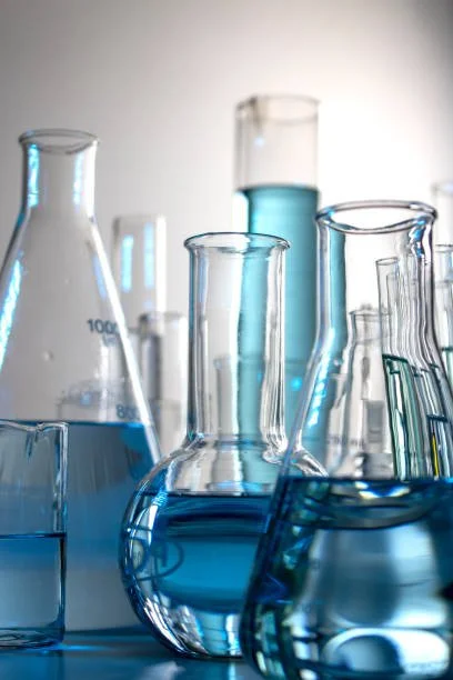 Several laboratory glassware containing blue liquid, including beakers, test tubes, and flasks on a white background.