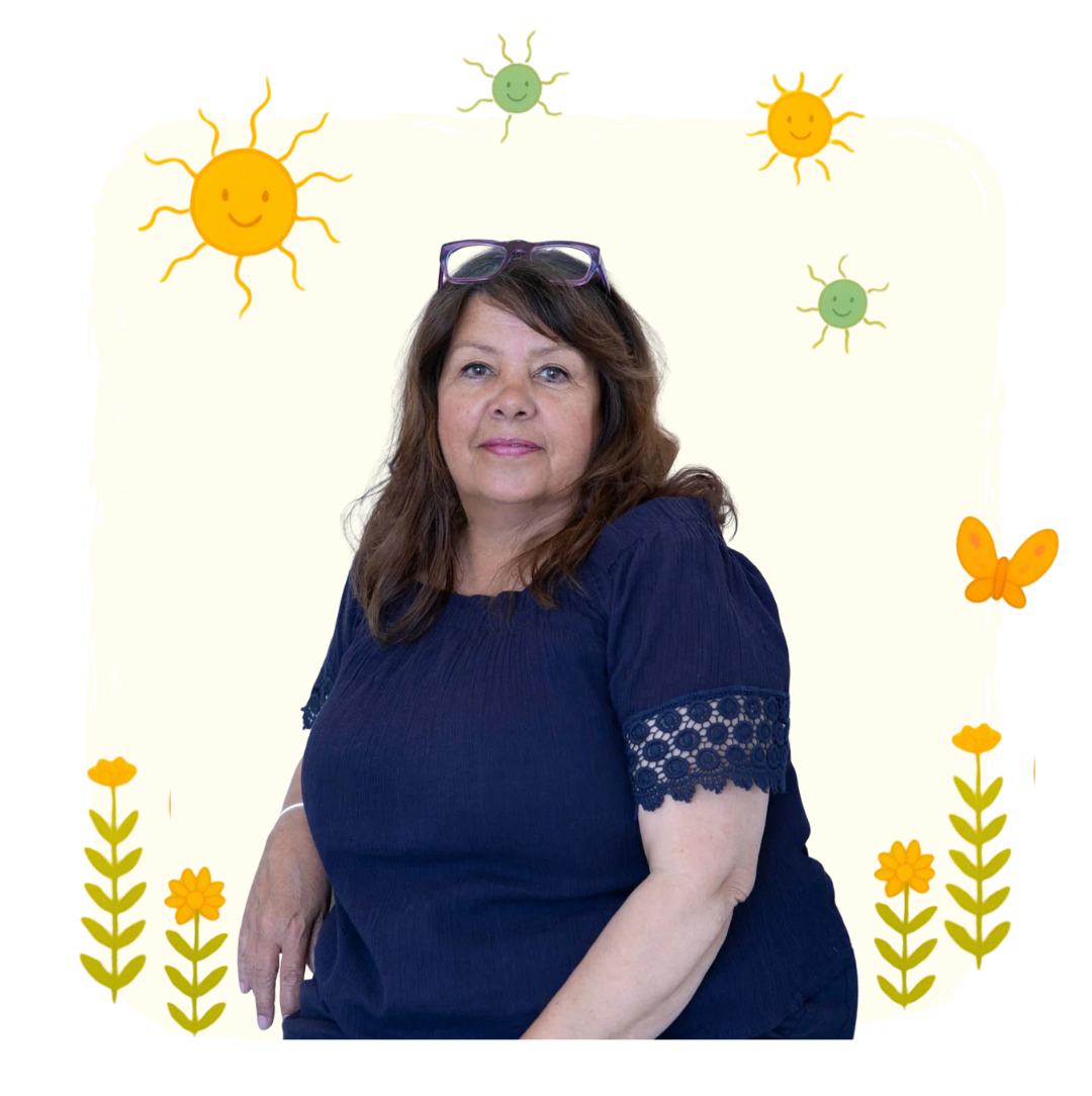 A woman with brown hair wearing a dark blue top, sitting in front of a light background decorated with cartoon suns, clouds, butterflies, and flowers.