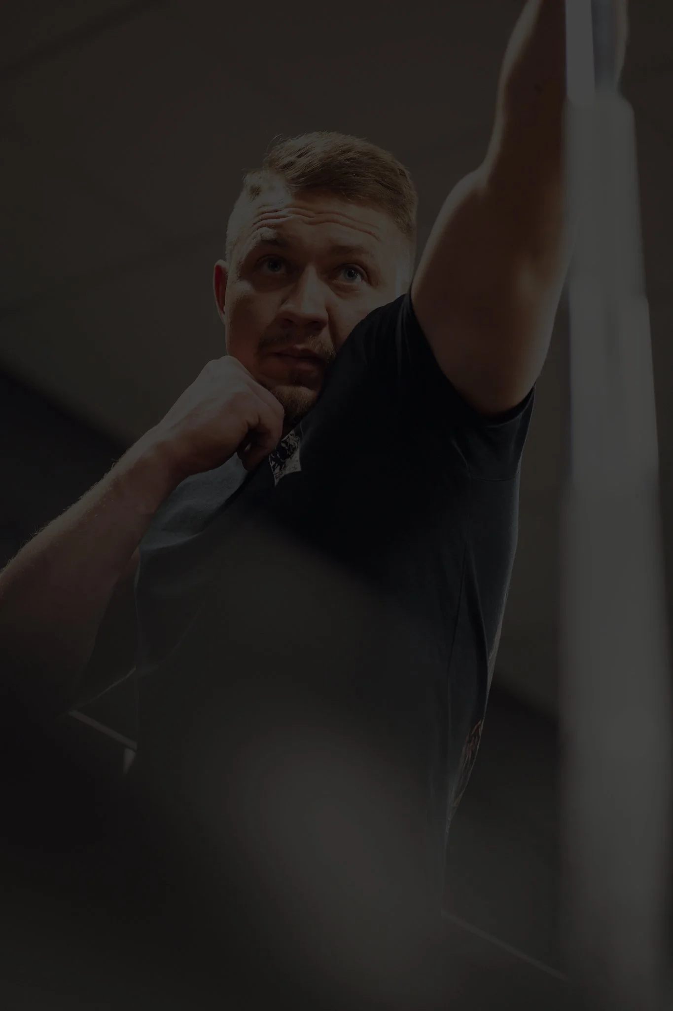 Ein Mann in einem schwarzen T-Shirt macht einen Kampfsport- oder Boxsatz, schaut konzentriert nach vorne.