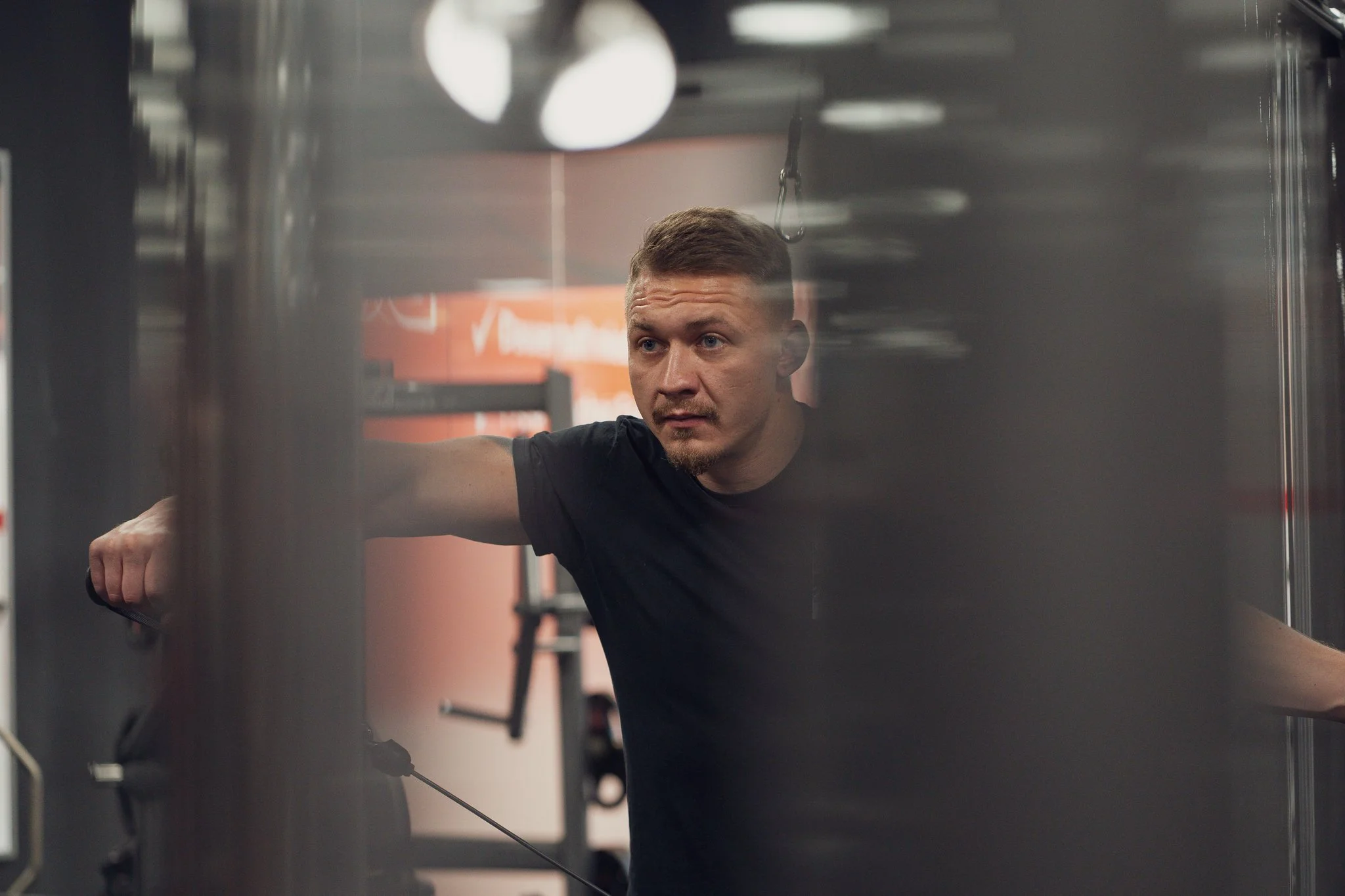 Mann trainiert im Fitnessstudio, blickt aufmerksam zur Seite, wear schwarze T-Shirt, im Hintergrund Fitnessgeräte.