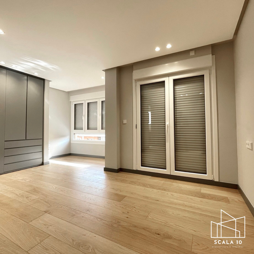 Habitación vacía con suelo de madera clara, ventanas con persianas enrollables y una puerta de vidrio con persiana instalada. Diseño moderno y luminoso.