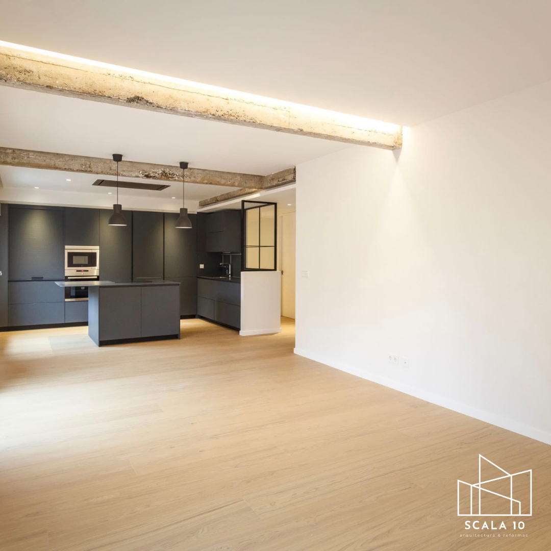 Espacio interior moderno y minimalista con cocina negra y paredes blancas, techos con vigas de concreto expuesto, y suelo de madera clara.