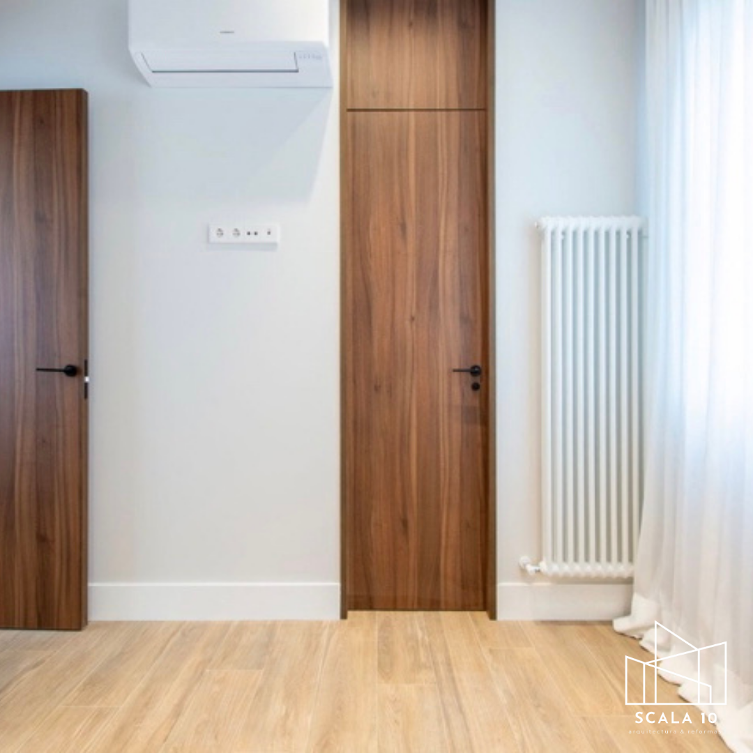 Habitación con paredes blancas, puertas de madera, radiador blanco, aire acondicionado y cortinas blancas en una ventana