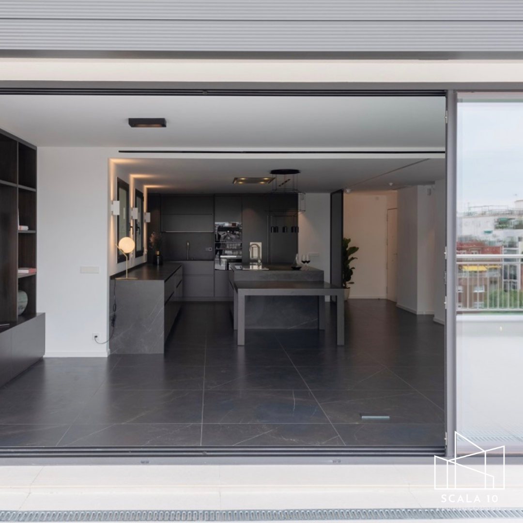 Cocina moderna con muebles grises, isla central y ventanas que se abren a un balcón.