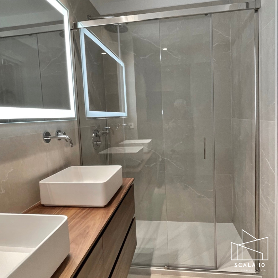 Baño moderno con ducha con puerta de vidrio, lavabo rectangular sobre mueble de madera y espejo con iluminación