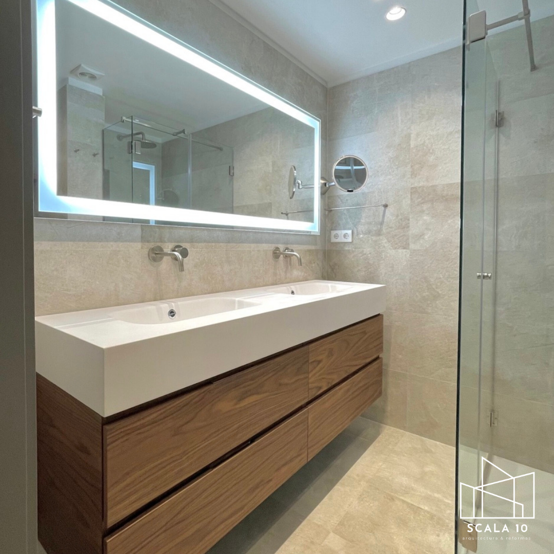 Baño moderno con lavabo doble, espejo con iluminación, pared de piedra, y ducha con puerta de cristal.
