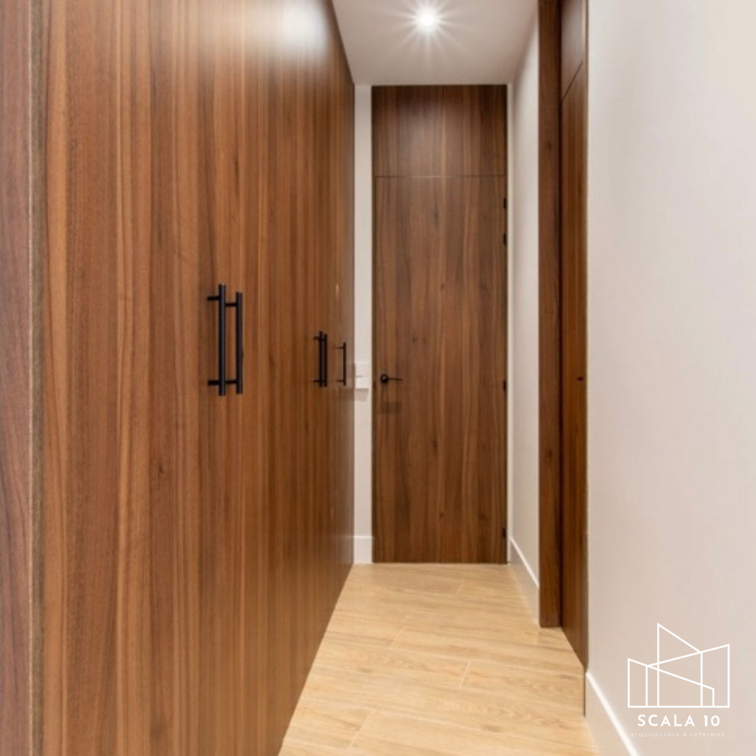 Pasillo con paredes y puertas de madera, piso de madera clara, luz en el techo, puerta al fondo.