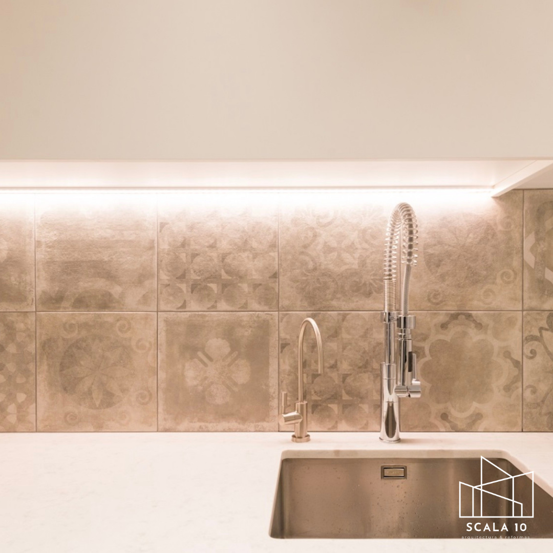 Encimera blanca con grifos de metal y azulejos decorativos en la pared.