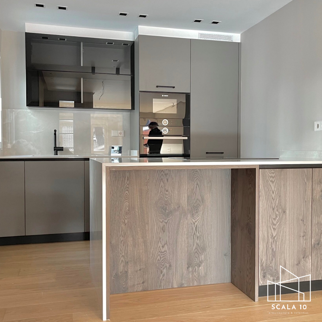 Cocina moderna con gabinetes grises, encimera blanca, isla de madera, horno empotrado y lavabo negro.