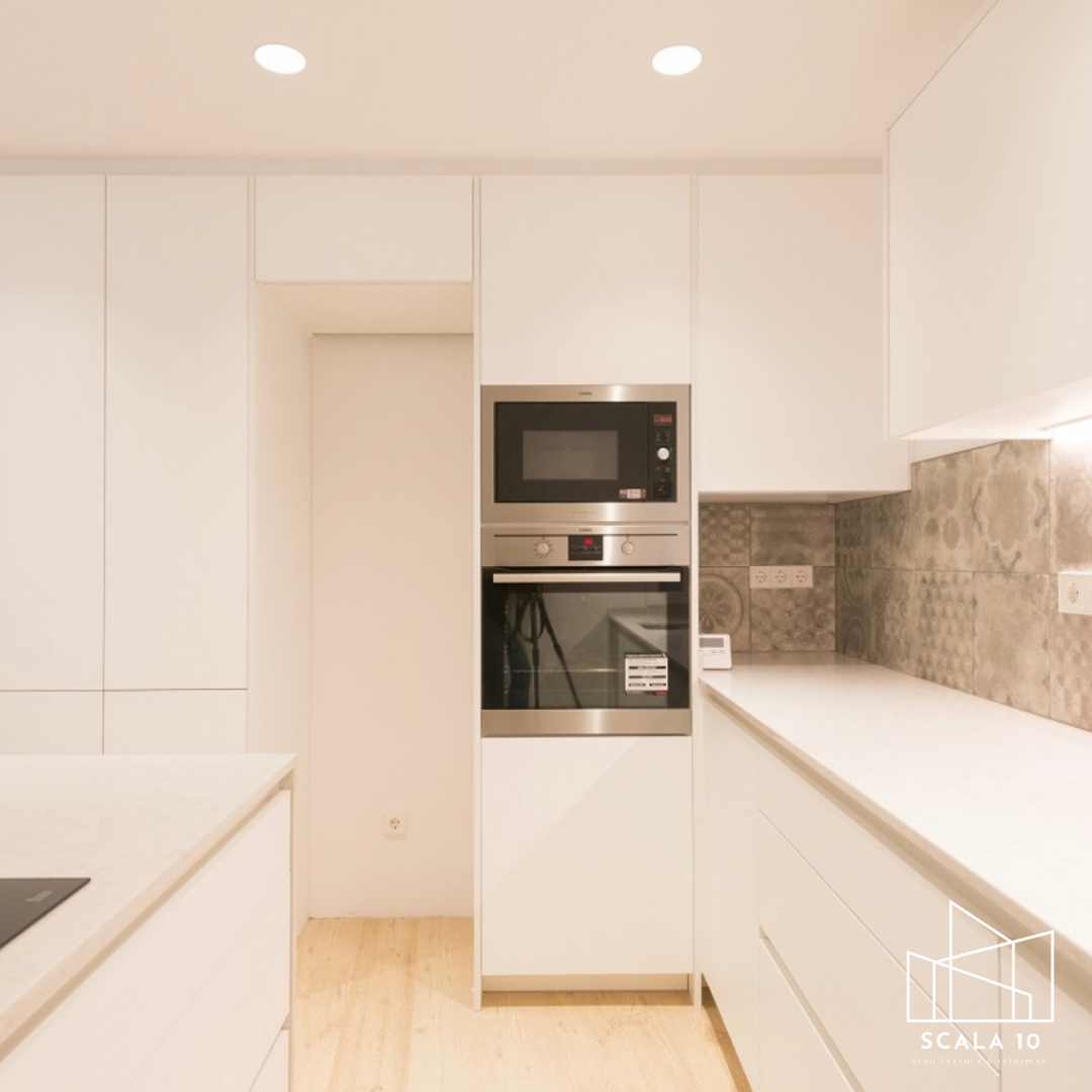 Cocina moderna con gabinetes blancos, encimera de piedra y electrodomésticos de acero inoxidable empotrados, incluyendo un microondas y un horno.