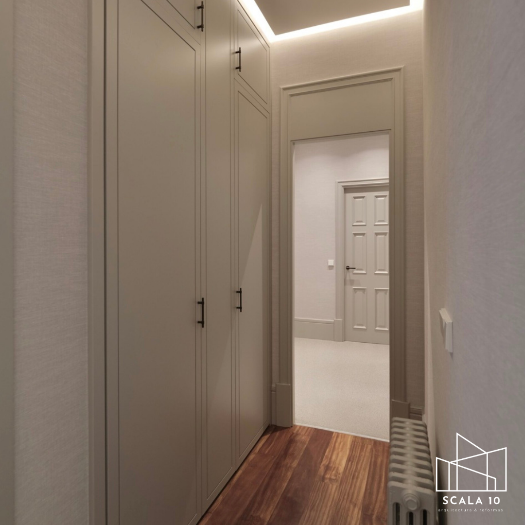 Vestidor y pasillo con closets empotrados blancos, puertas y molduras decorativas en tonos claros, techo con iluminación LED, piso de madera y radiador al costado.