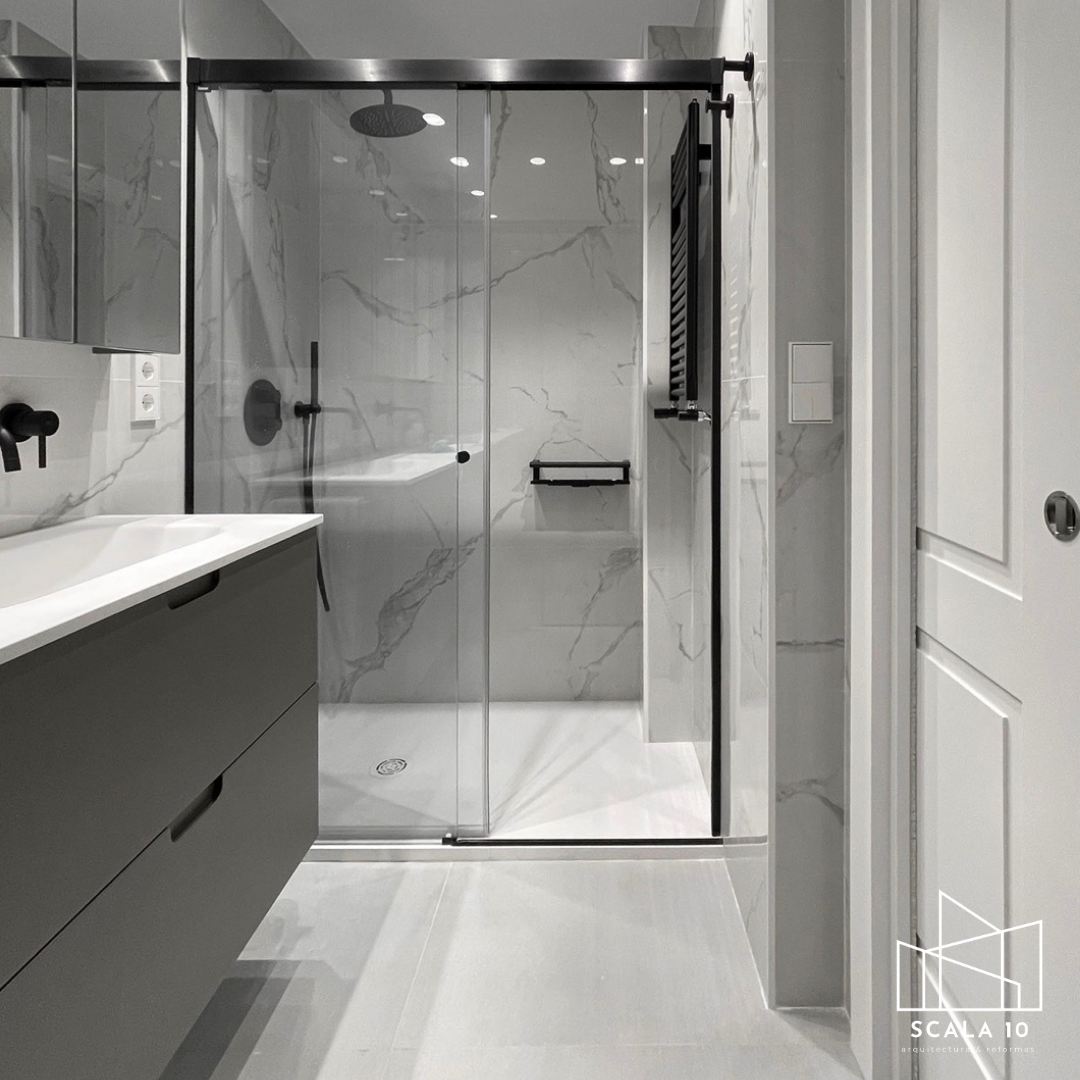 Baño moderno con paredes de mármol y ducha de vidrio con accesorios negros.