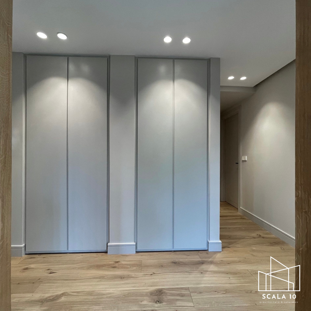 Puertas de armario blancas en una pared, en un espacio interior con suelo de madera y luces empotradas en el techo.