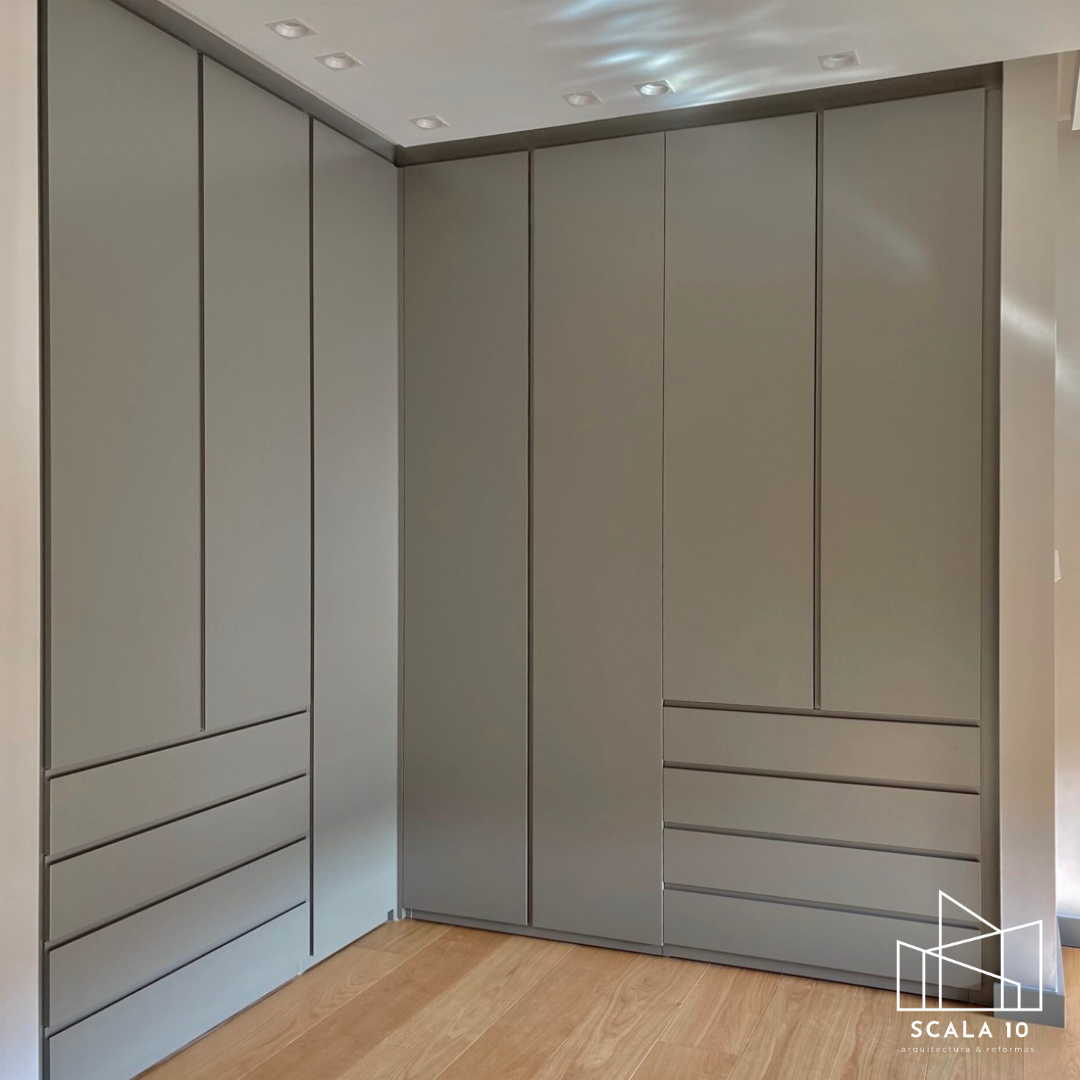 Armario moderno gris con puertas y gavetas, en una habitación con suelo de madera y techo con luces empotradas.