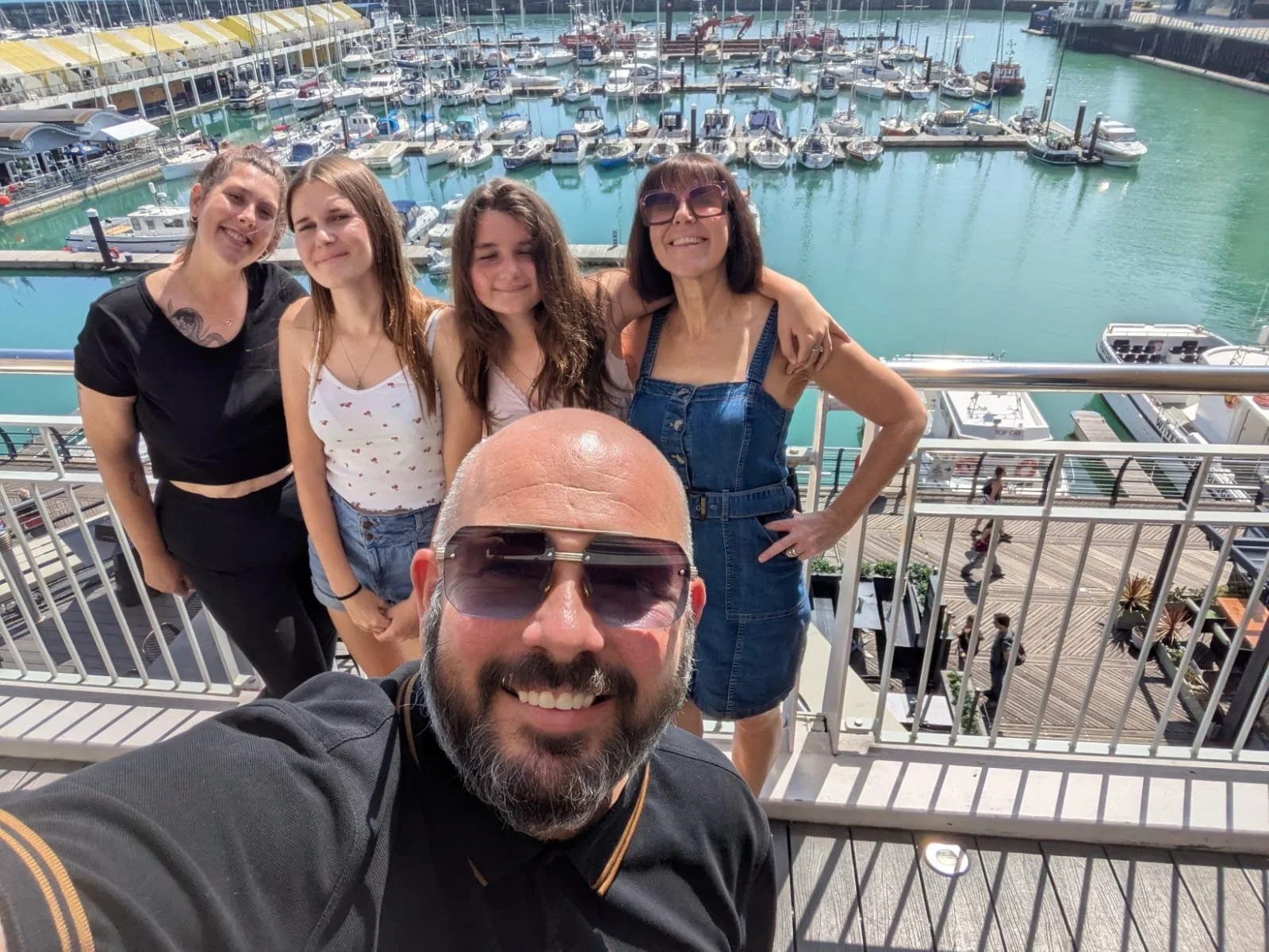 A group of five people, including four women and one man, taking a selfie on a balcony overlooking a marina with numerous docked boats and yachts. Newhaven Pub & Restaurant