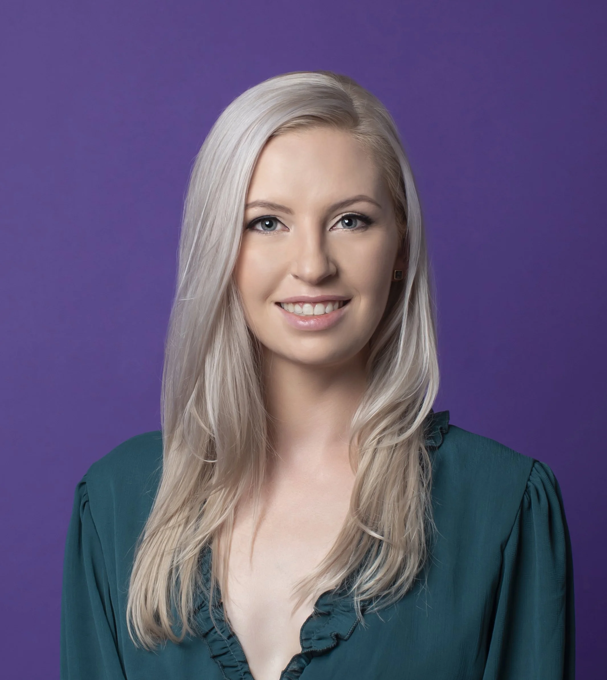 Portrait of a Jordan Blair, the host of Dreamful Bedtime Stories podcast, a young woman with long blonde hair and blue eyes, smiling, wearing a teal blouse with ruffled collar, against a purple background.