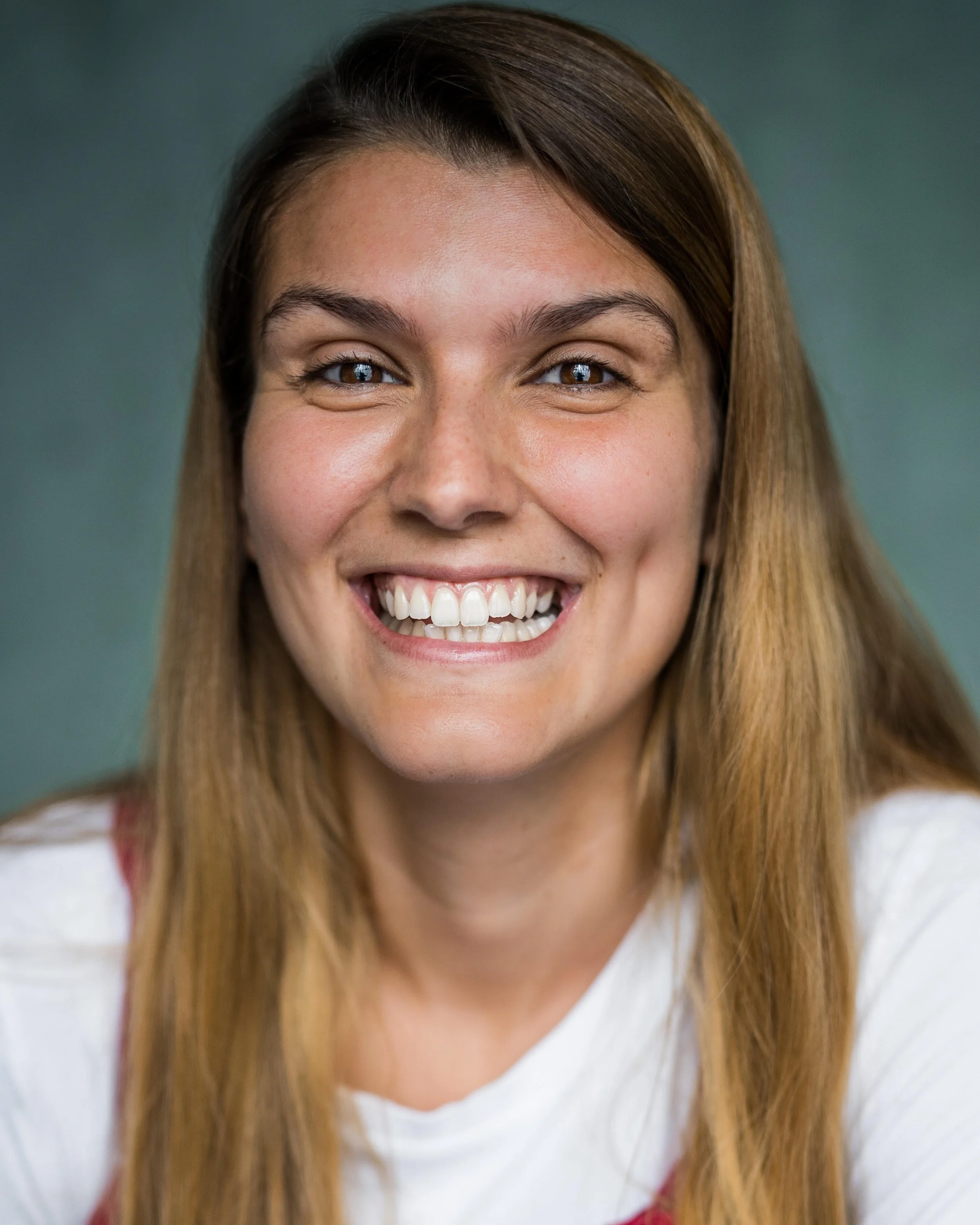 Close-up of smiling young woman with straight brown hair against a green background.