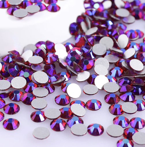 Multicolored rhinestones and silver backings scattered on a white surface.