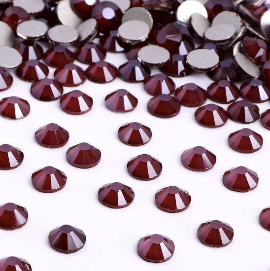 Multiple small red rhinestones scattered on a white surface with some piled up in the background.