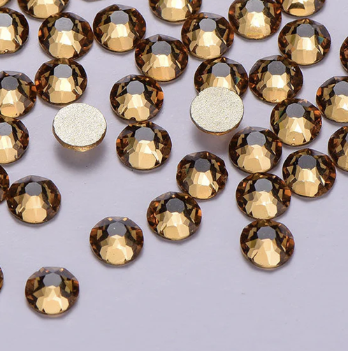 Collection of small, round, faceted, brownish gold rhinestones scattered on a light gray surface.