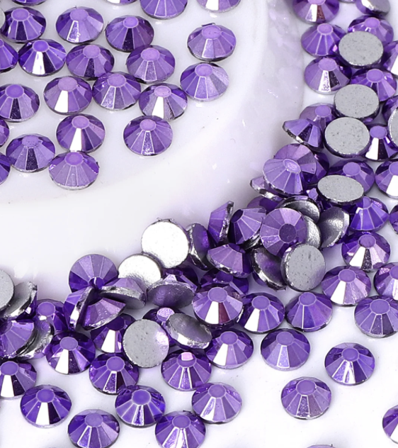 Collection of purple rhinestones scattered on a white surface.
