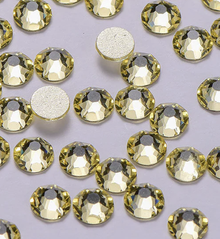 Close-up of numerous yellow rhinestones scattered on a white surface, with two glittering round backing pieces visible.
