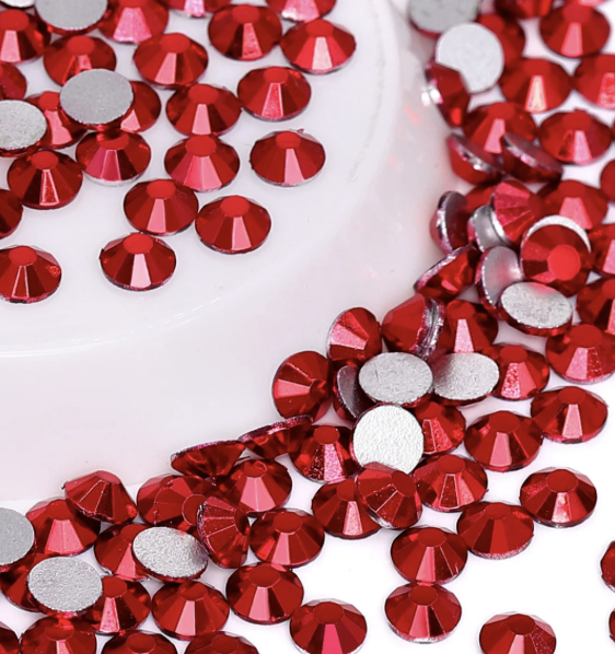 Close-up of red rhinestones scattered on a white surface, with part of a white circular object in the background.