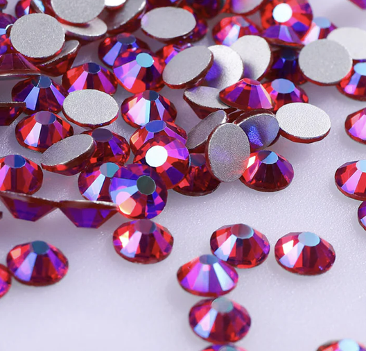 A collection of red and purple rhinestones with flat grey backs on a white surface.