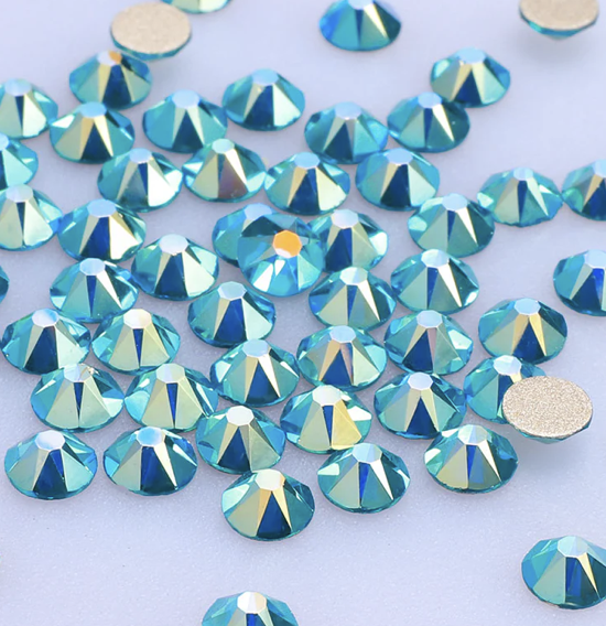 A close-up view of numerous blue and iridescent rhinestones scattered on a light surface.