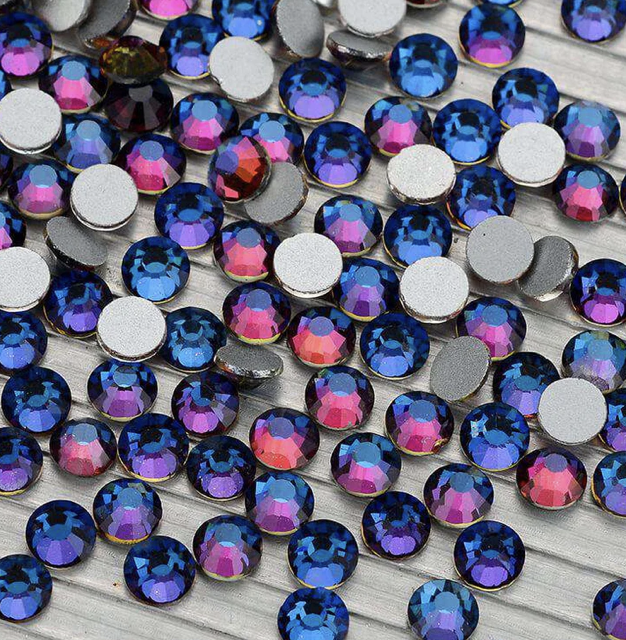 Close-up of multicolored rhinestones with flat silver backing on a wooden surface.