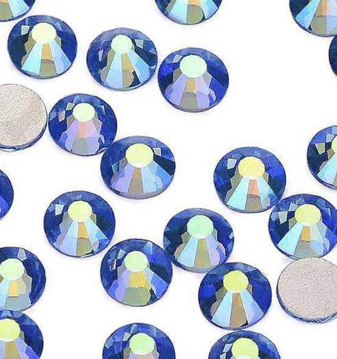 Multiple blue and iridescent rhinestones scattered on a white background, with two visible silver backing pins.