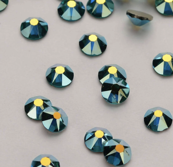 Several small blue and yellow rhinestones scattered on a gray surface, with one rhinestone that is broken.