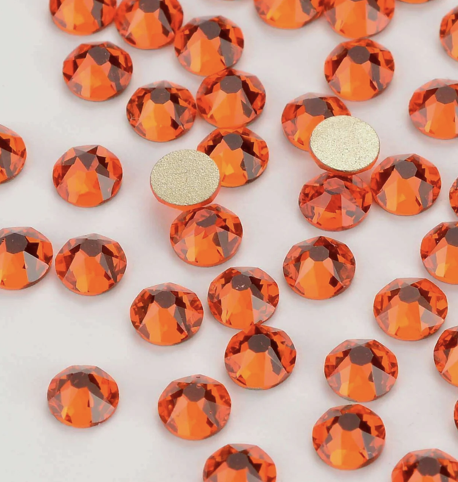 Close-up of multiple orange rhinestones and two adhesive-backed rhinestones on a white surface.