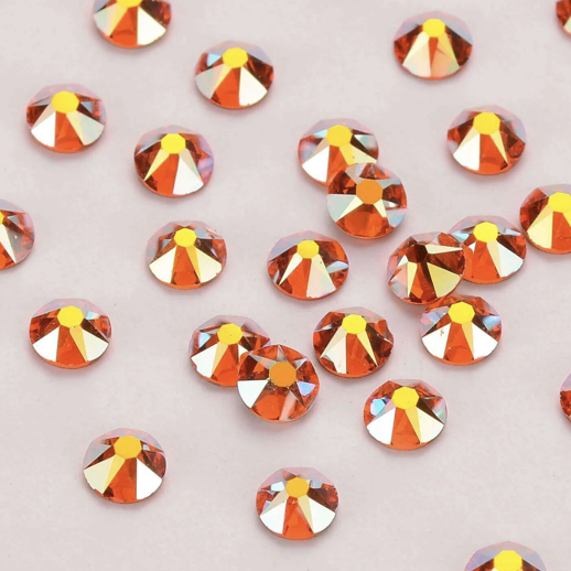 Collection of orange rhinestones with yellow accents scattered on a light purple background.